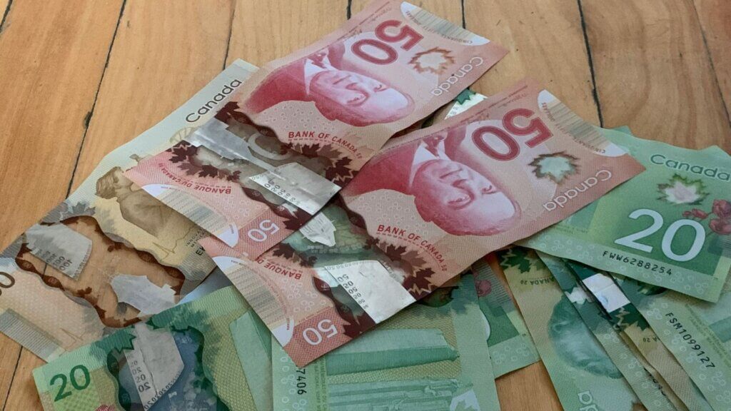 A scattered pile of Canadian paper money including 50 and 20 dollar bills resting on a wooden floor.
