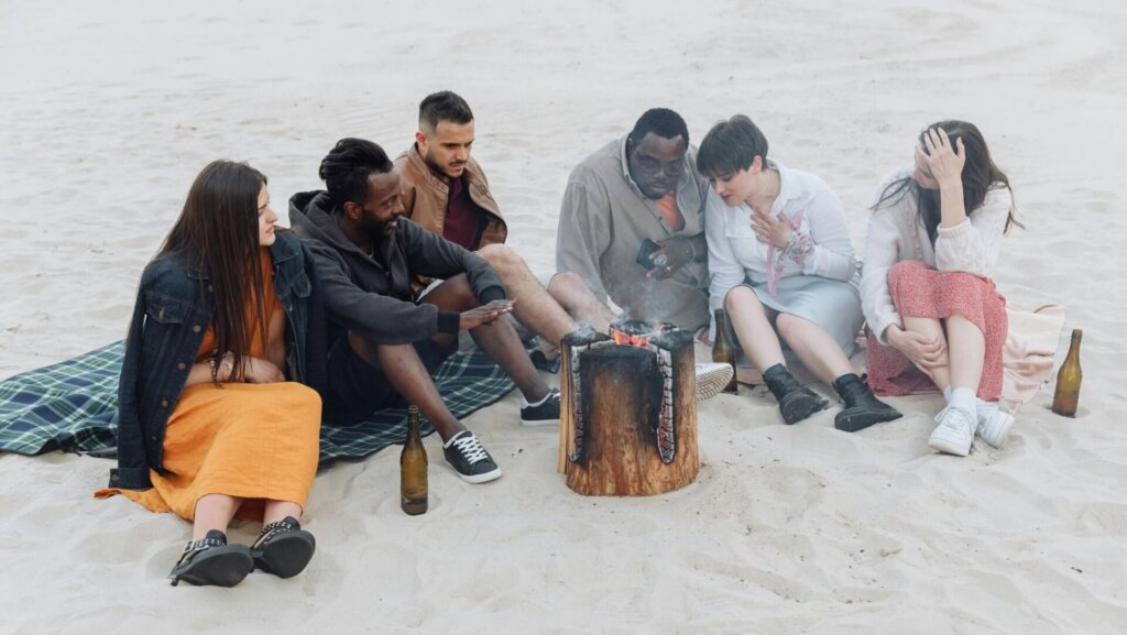 Group of people sitting together on sandy beach near the shoreline.