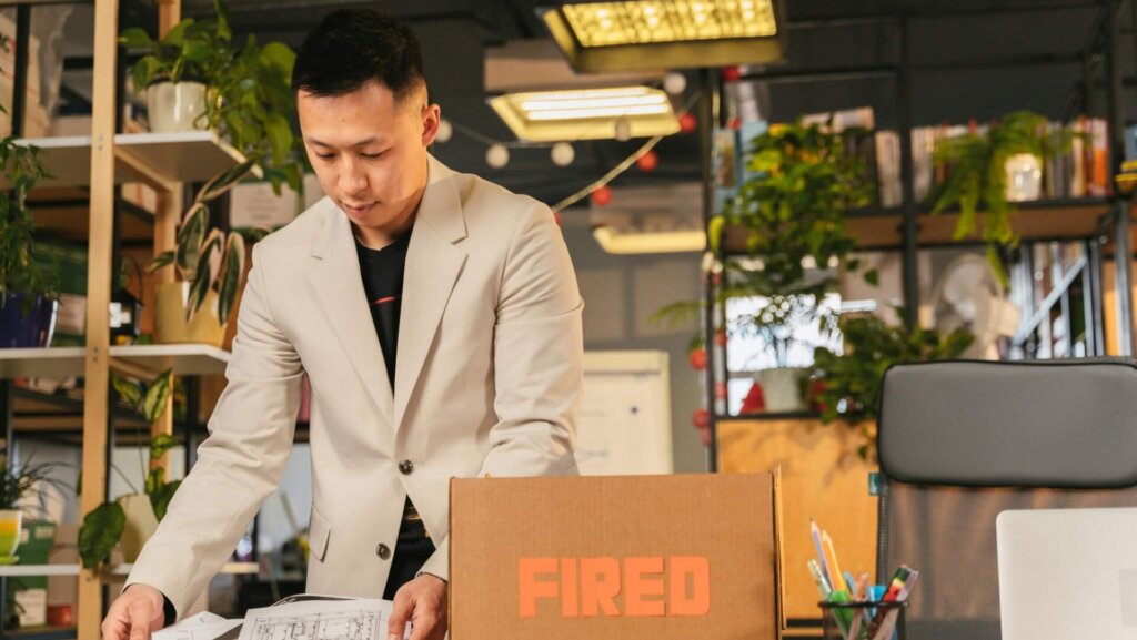 A man packing personal belongings into a box at an office desk, conveying job loss or termination.