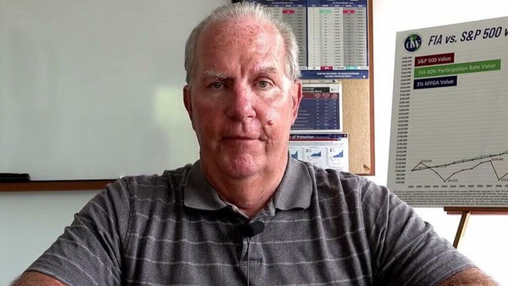 Dan White, founder of Daniel A. White & Associates, sits facing the camera in an office setting with financial charts and graphs displayed behind him.