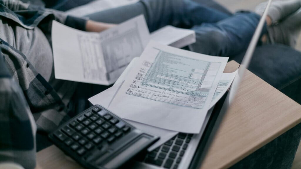 Utility bills placed on sofa next to open laptop and calculator.