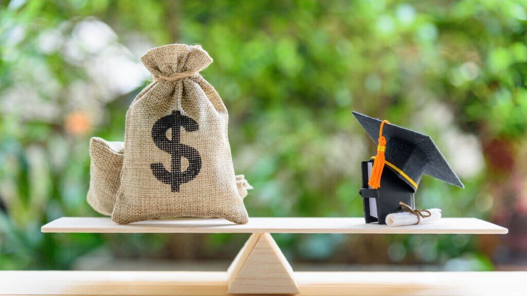 Graduation cap placed beside stacked coins and paper money.