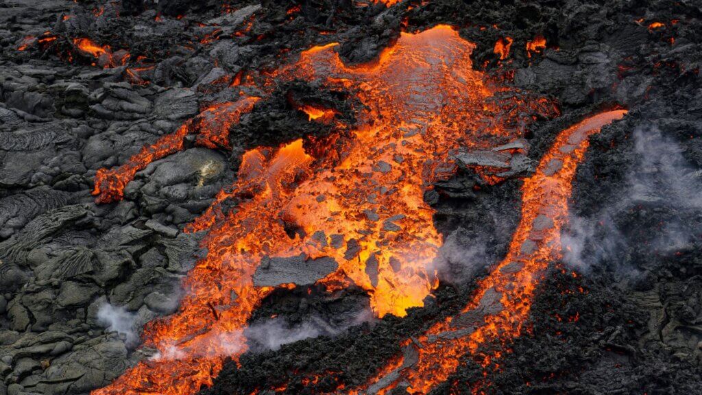 Bright lava flow moving across volcanic rock surface