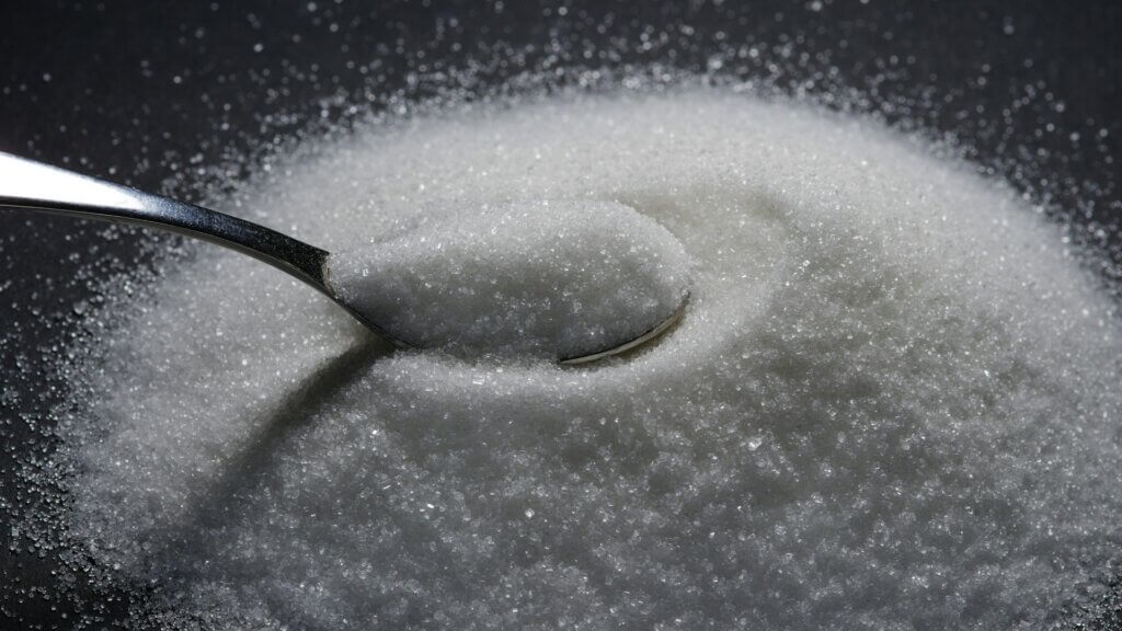Spoon filled with granulated sugar resting on a table