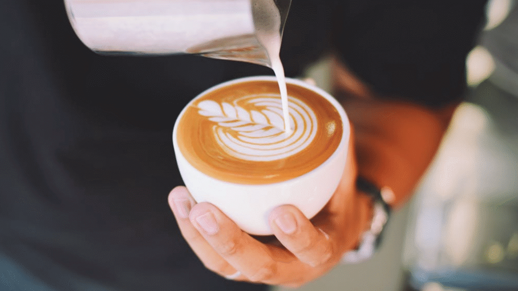 a hand holding a cup of coffee while pouring milk on it
