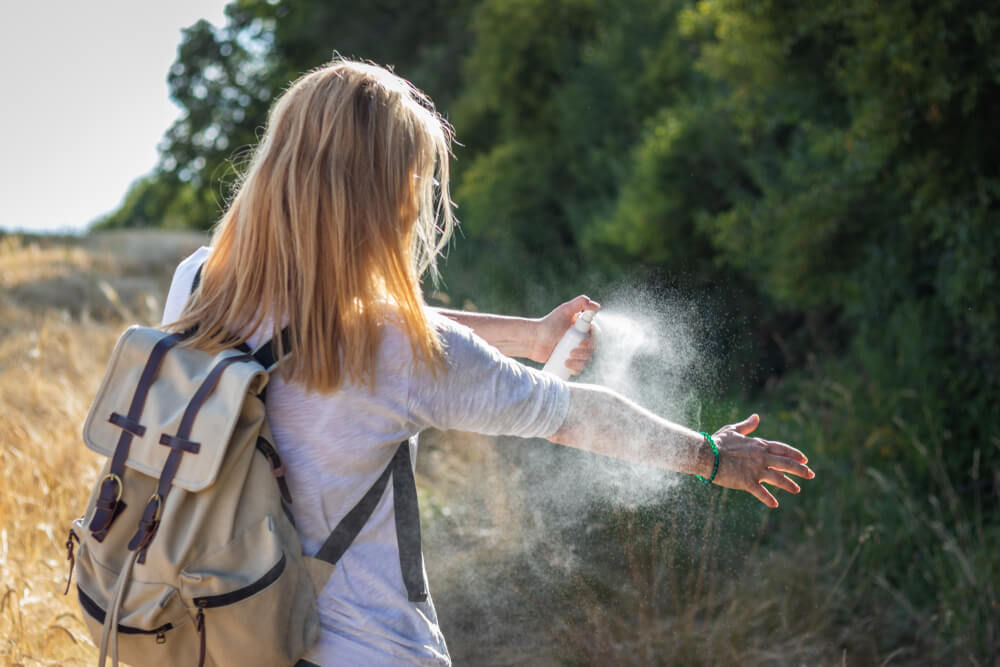 A woman outdoors spraying tick repellent on their arm while hiking.