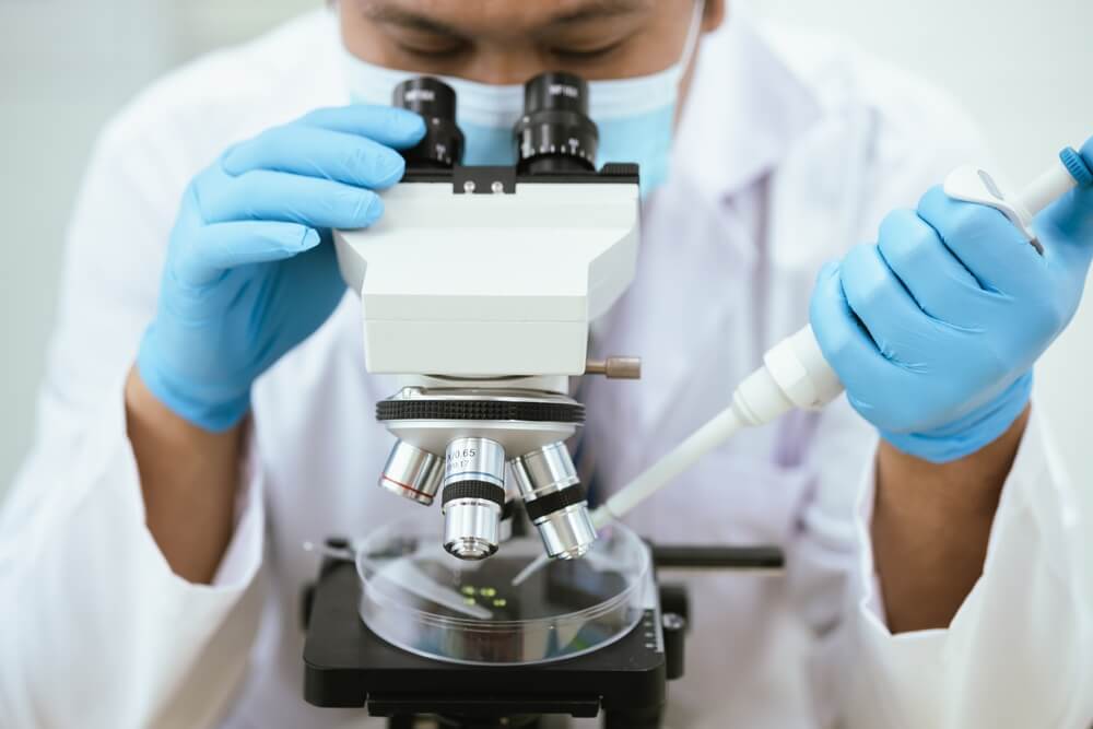 Scientist examining samples under a microscope while using a pipette in a medical research laboratory.