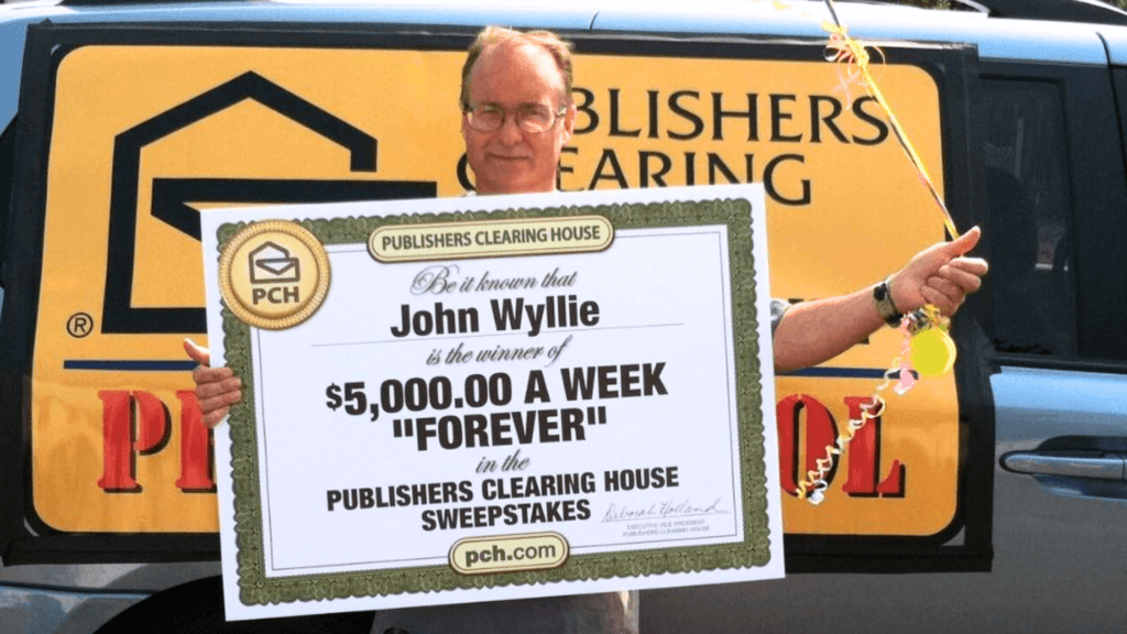 John Wyllie holding a large Publishers Clearing House prize board for a "$5,000.00 A Week Forever" sweepstakes win.