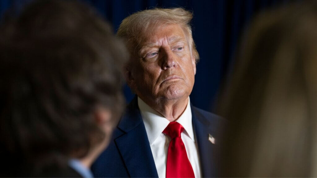 Donald Trump listening during a meeting, wearing a red tie and dark suit.