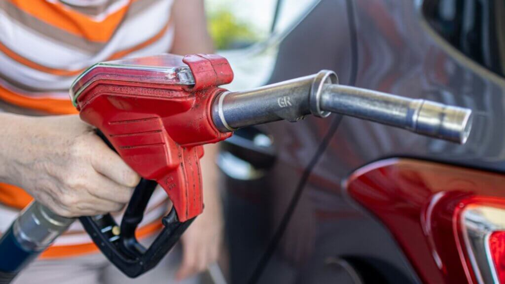 A person holding a red gasoline nozzle about to refuel their car.