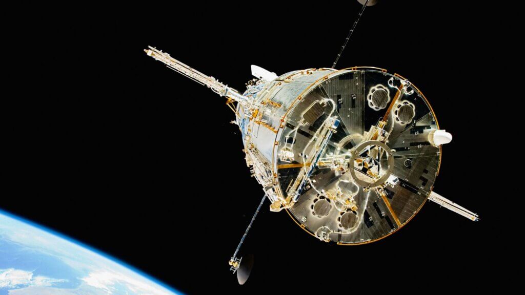 Satellite in orbit above Earth with visible planet curvature against black space.