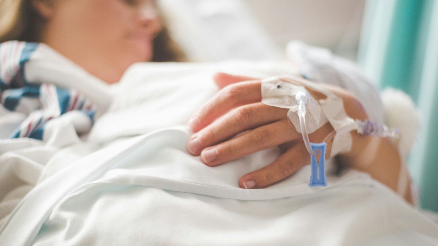 Patient lying in a hospital bed with an IV line inserted in their hand.