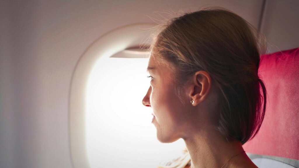 Woman seated by an airplane window looking outside during a flight.