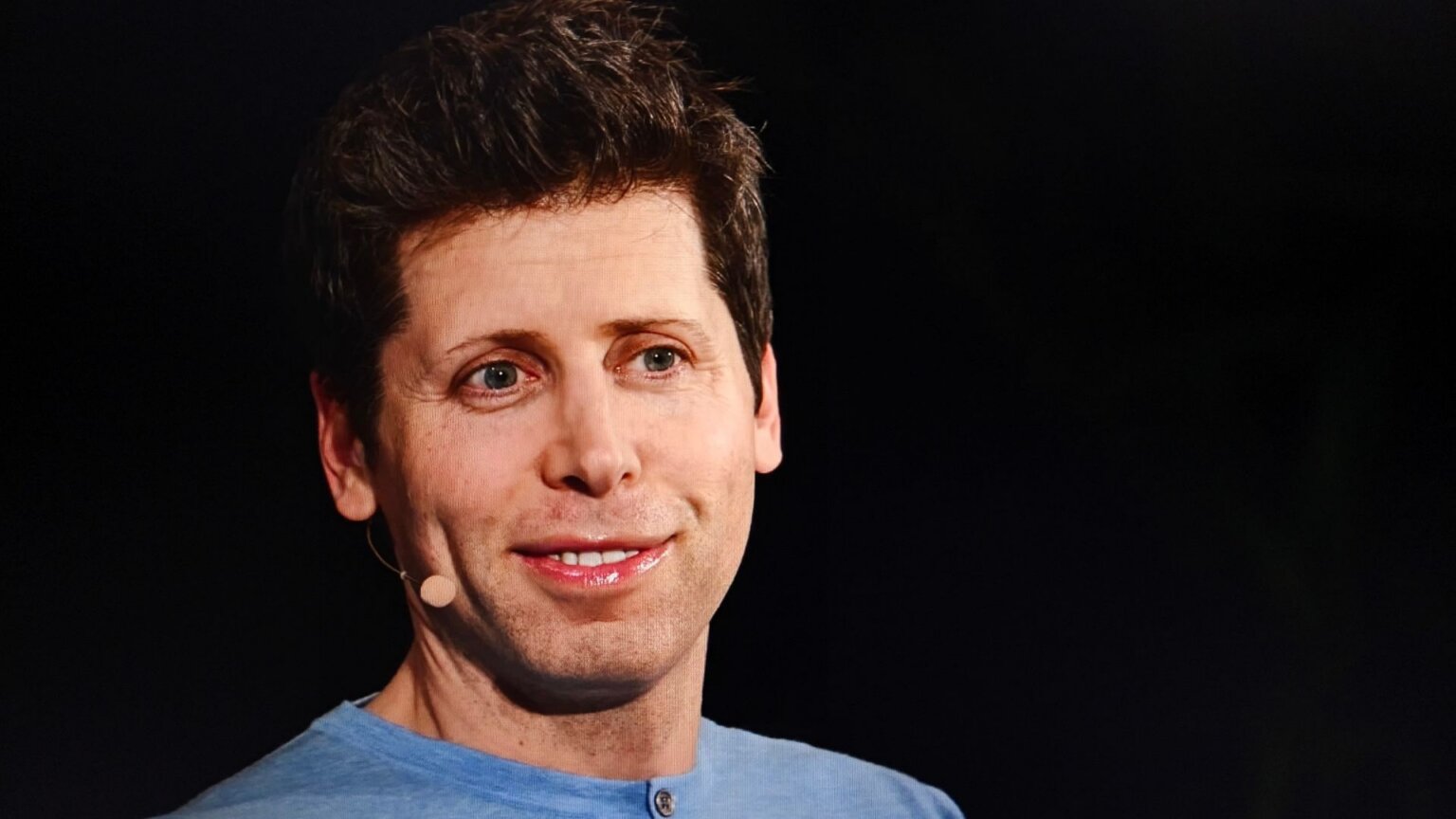 Sam Altman speaking onstage while wearing a headset microphone.