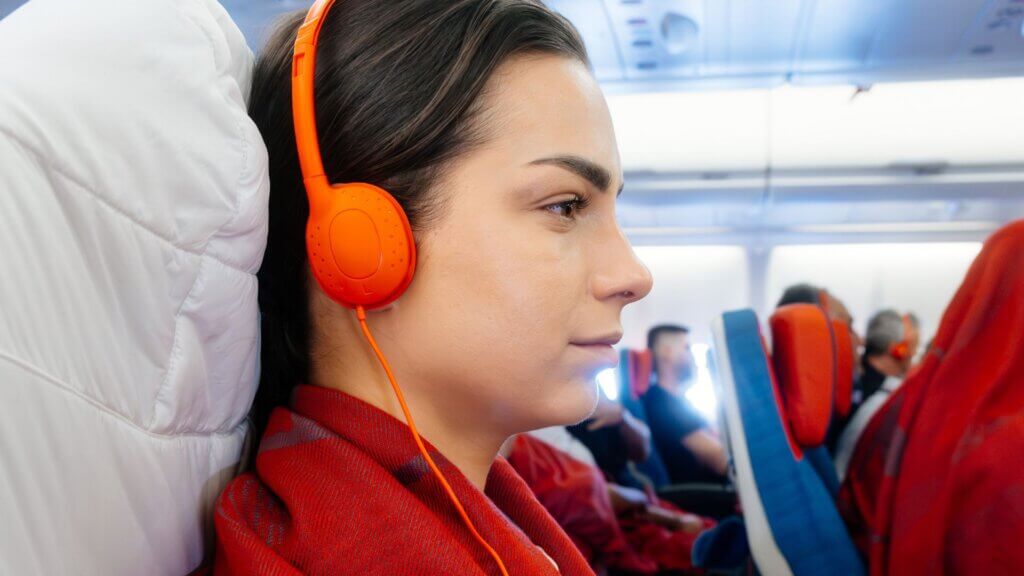 Passenger wearing bright orange headphones while seated on an airplane.