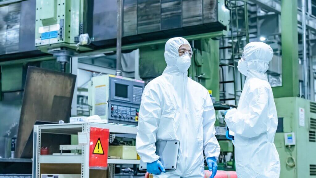 Two lab workers in protective hazmat suits inside an industrial research facility.