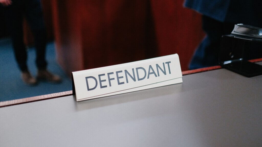 Close-up of a desk sign labeled “Defendant” in a courtroom setting.