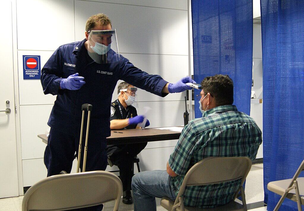 U.S. Coast Guard personnel conduct a temperature screening of a traveler during a health checkpoint.