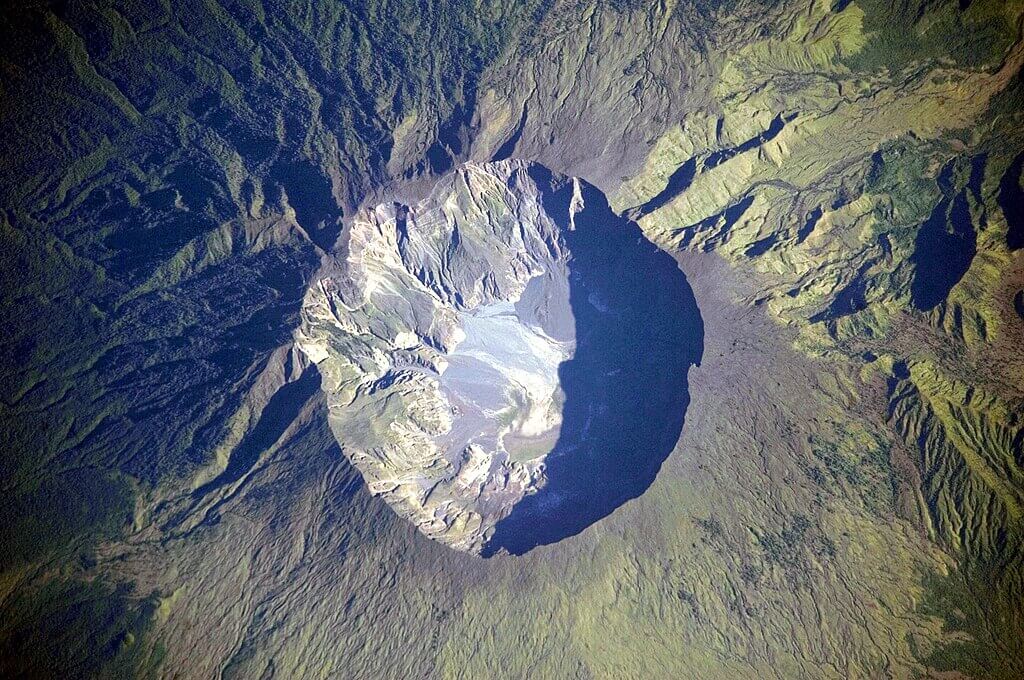 Aerial view of a dormant volcanic crater with steep rocky walls and a barren basin.