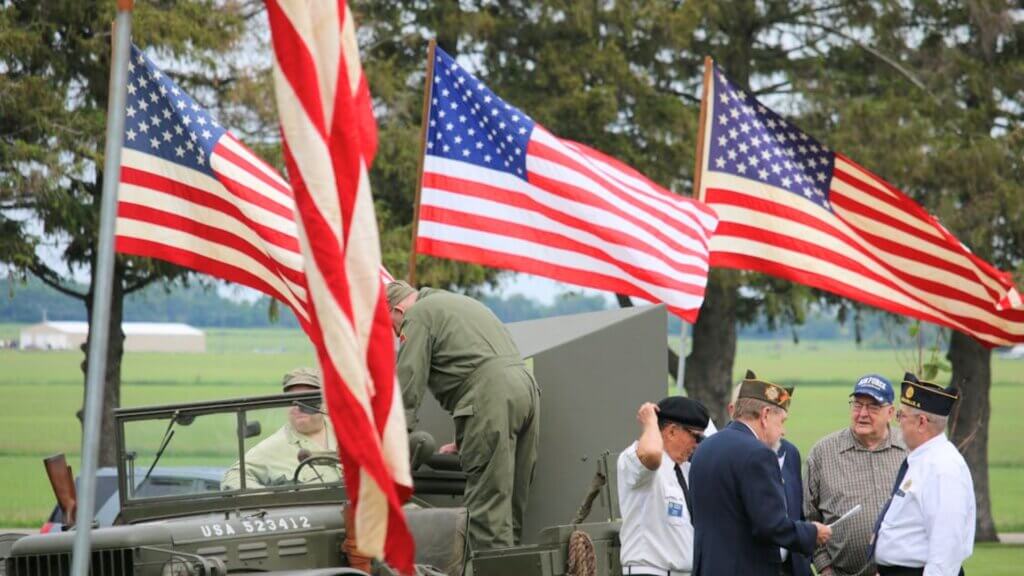 Veterans standing near a military vehicle with American flags.