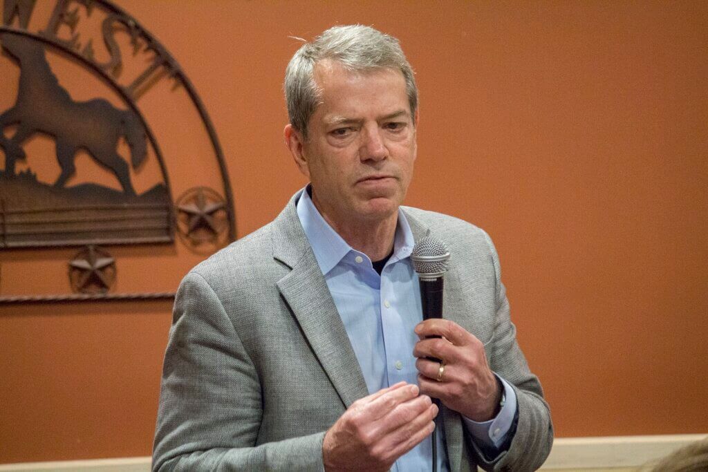 Governor Jim Pillen speaking into a handheld microphone during a public event.