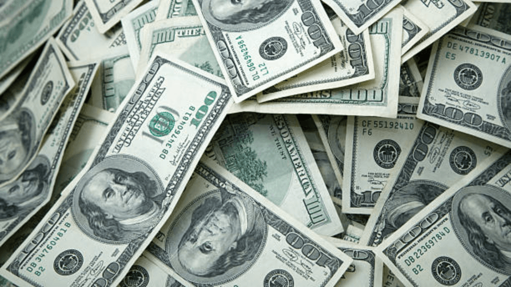 A large, scattered pile of one-hundred-dollar bills.