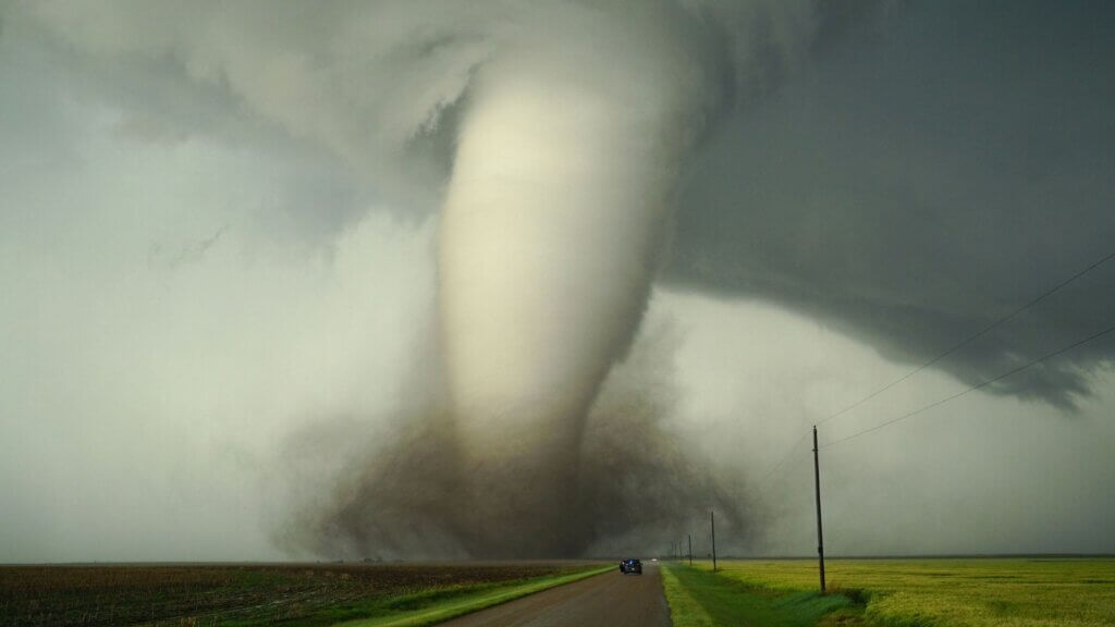 Large tornado funnel forming over rural road and farmland during severe storm.