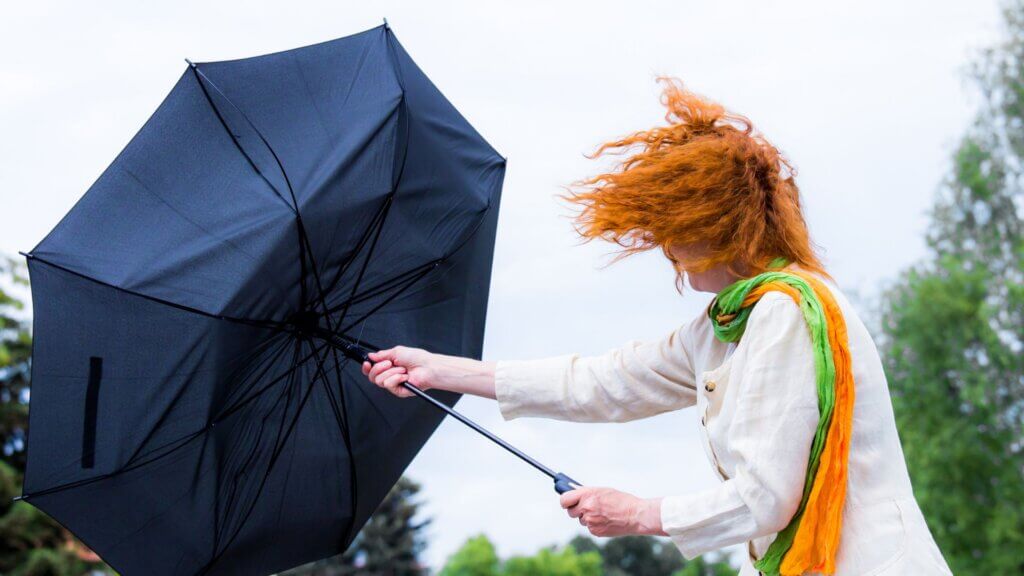 Woman struggling to hold an umbrella as strong wind blows it inside out.