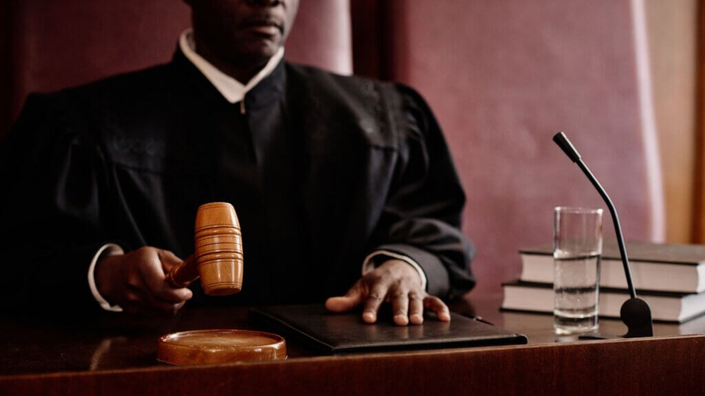 Judge holding a gavel while seated at a courtroom bench during a legal proceeding.