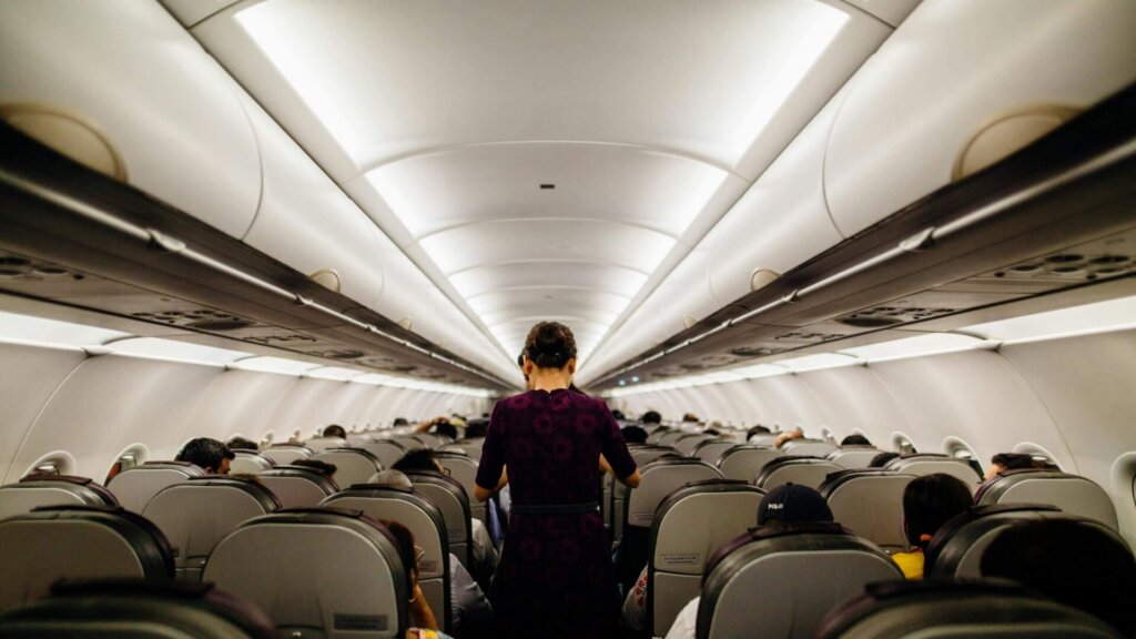 Passenger standing in the aisle inside a commercial airplane cabin.