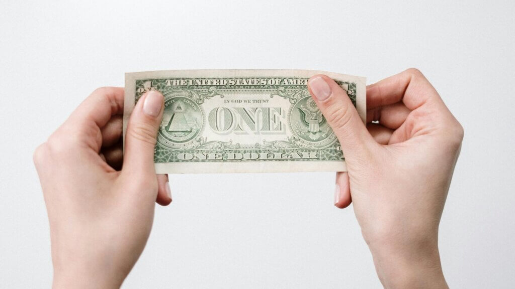 Hands holding a one-dollar bill against a plain background.