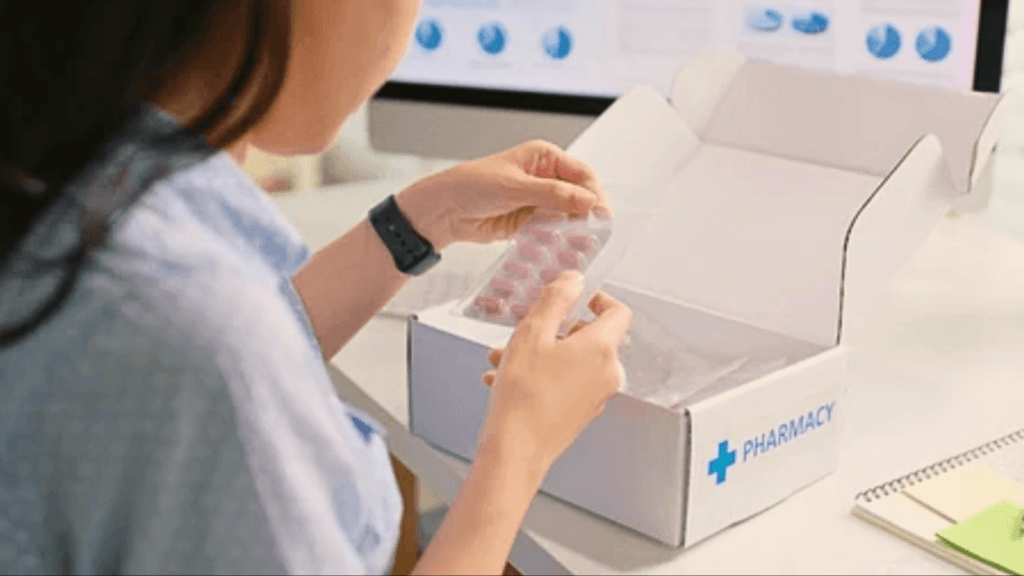 A person opening a white pharmacy delivery box and holding a blister pack of red medication tablets.