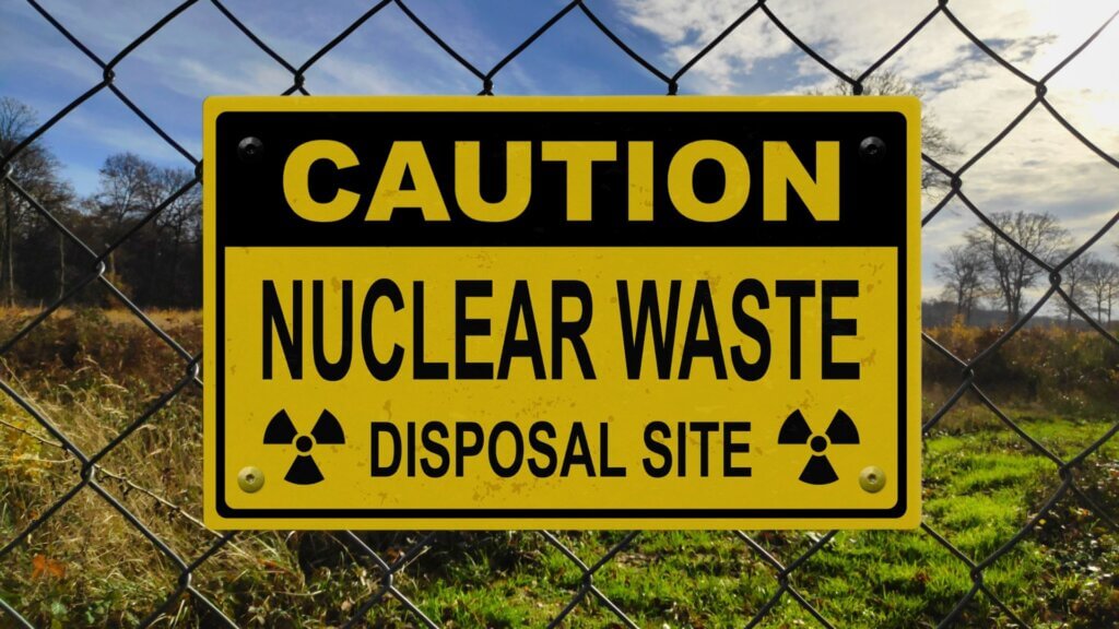 Yellow nuclear waste disposal caution sign attached to a chain link fence.