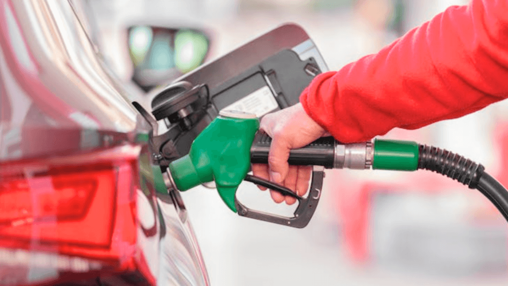 A person holds a green nozzle to pump gas into a car.