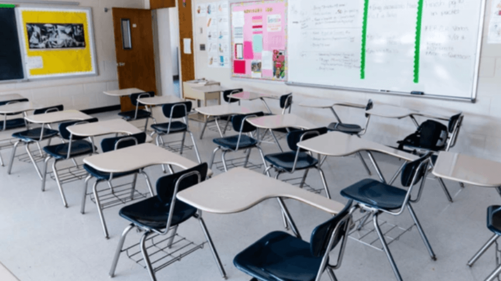 An empty, modern classroom with several rows of blue and beige student desks and a whiteboard.