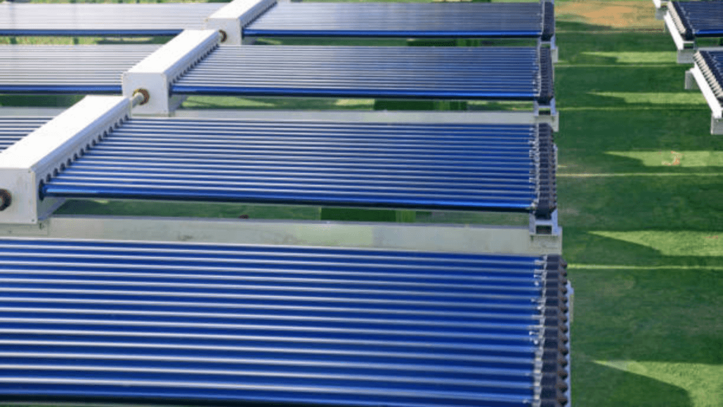 A close-up view of an array of industrial evacuated tube solar collectors installed on a grassy field, designed for high-efficiency solar water heating.