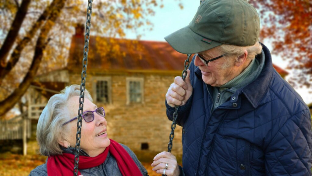 Man standing beside a woman sitting on a swing outdoors.