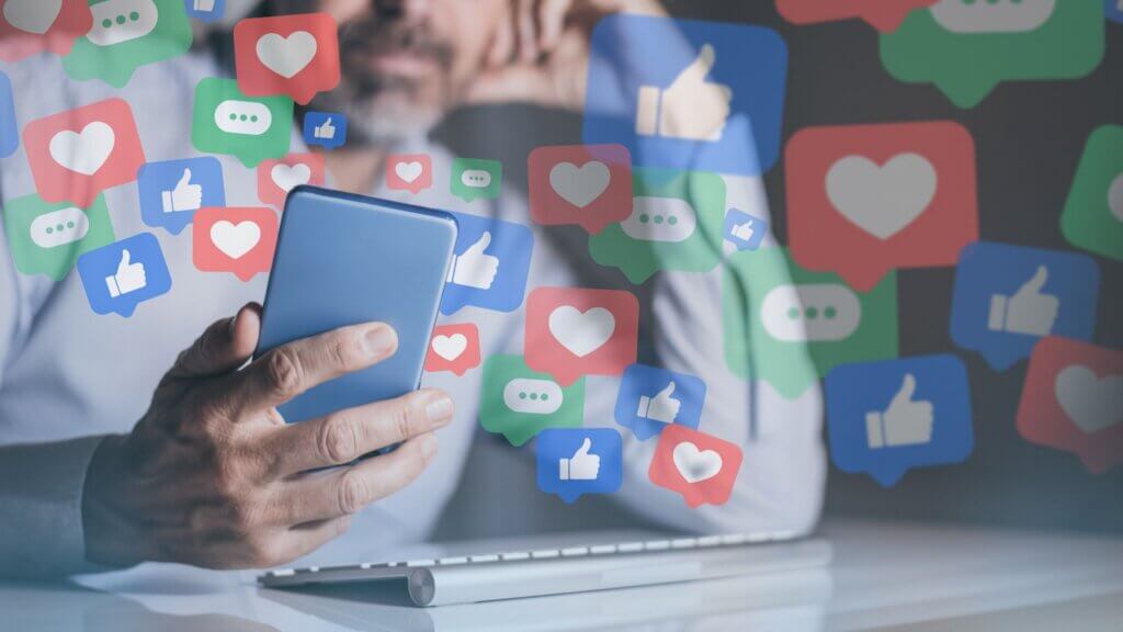 Person holding smartphone with floating social media reaction icons.