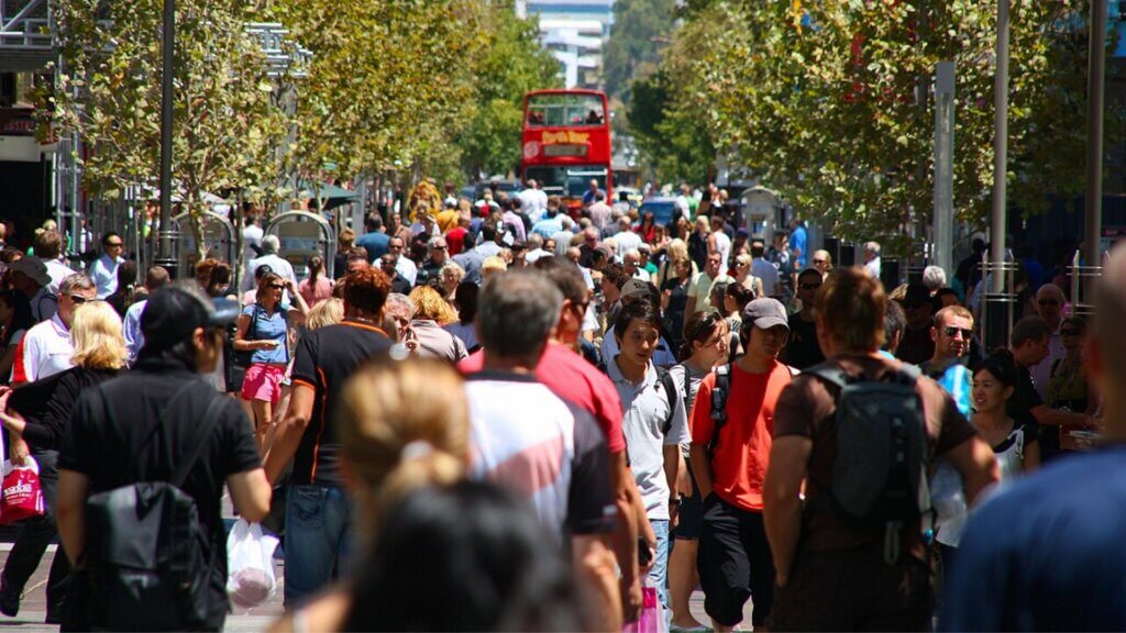 Crowded city street with pedestrians and a red double-decker bus, illustrating a busy public area.