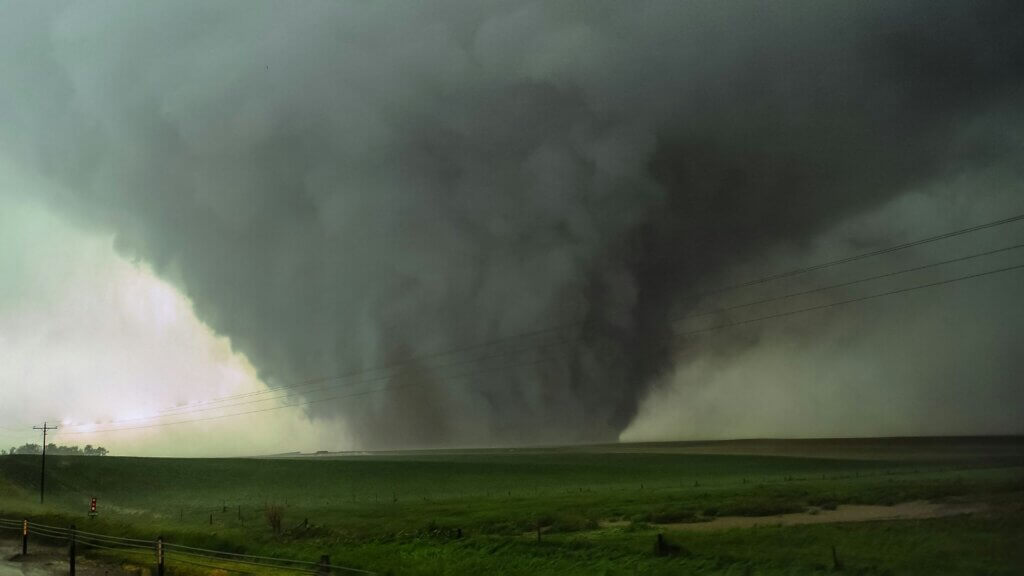 Large tornado funnel descending from a dark storm cloud over a flat rural field.