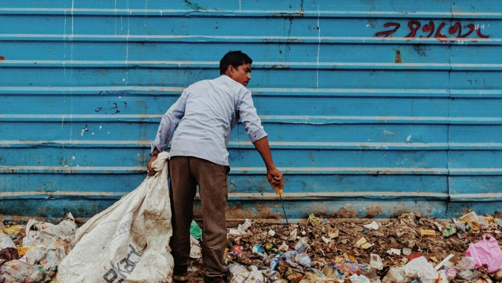 Worker gathering waste near a construction fence in an urban area.