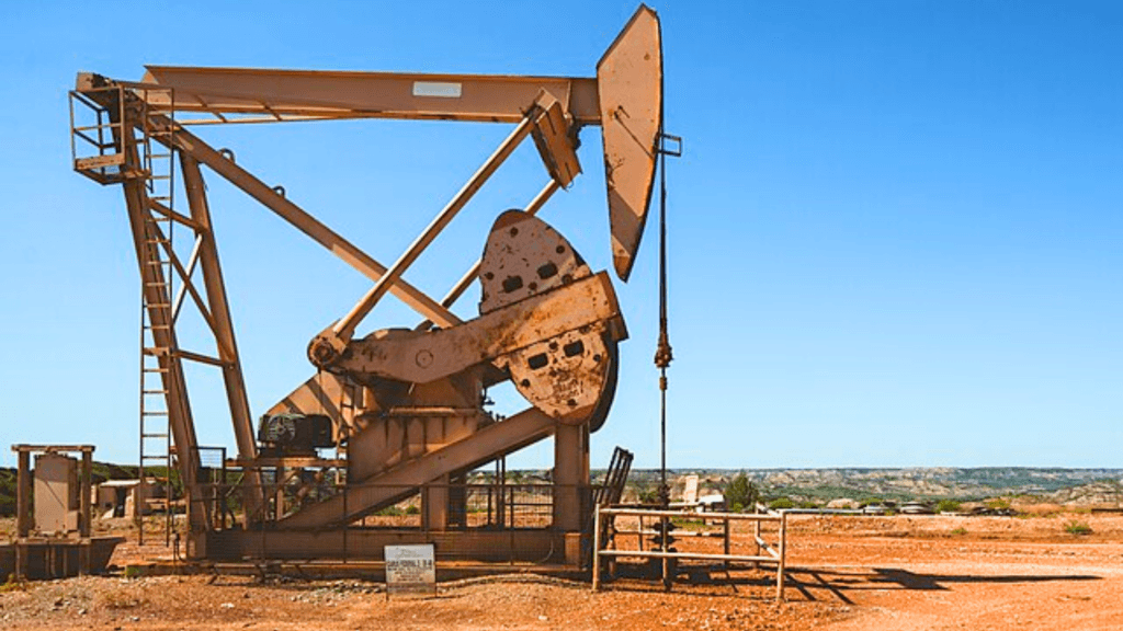A large metal oil pump stands in a dry dirt field.