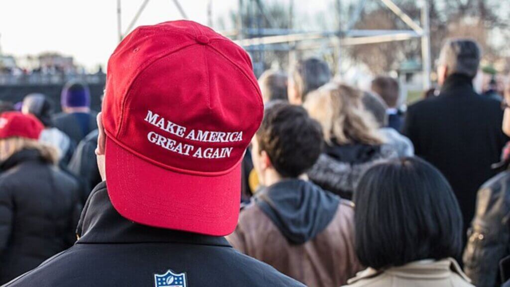 Person wearing a red “Make America Great Again” hat at a crowded outdoor event.