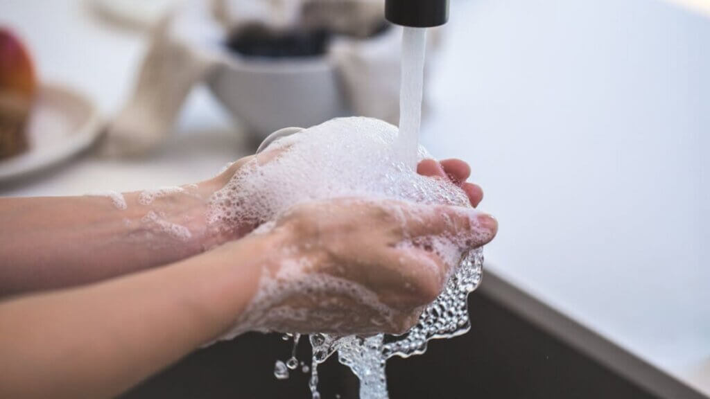 Person washing hands with soap under running water at a sink.