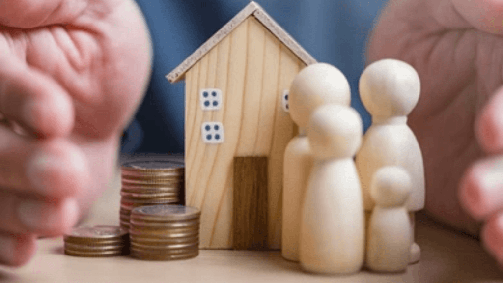 Hands cupping a small wooden house model next to stacks of coins and wooden peg figures representing a family.