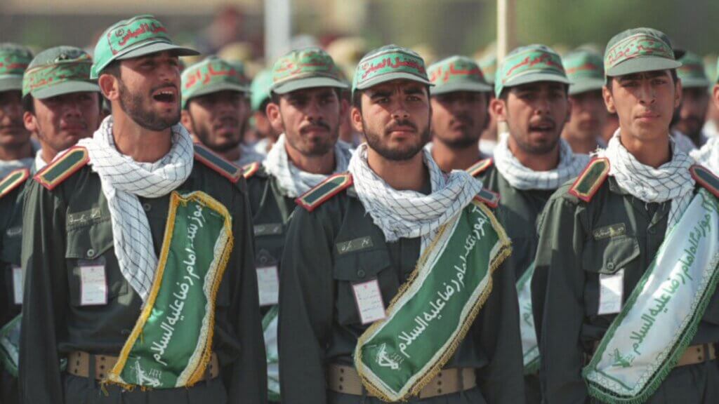 Iranian Revolutionary Guard members standing in formation wearing green uniforms and caps during a military gathering.
