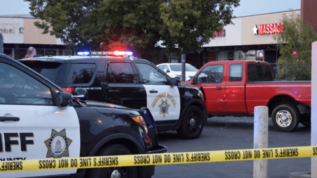 Police and Highway Patrol vehicles with flashing lights parked behind yellow tape at a cordoned-off scene.