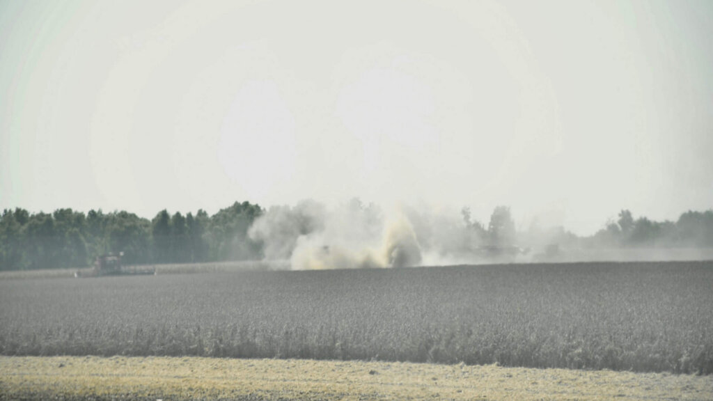 Tractor harvesting crops in a dusty field during farm work.