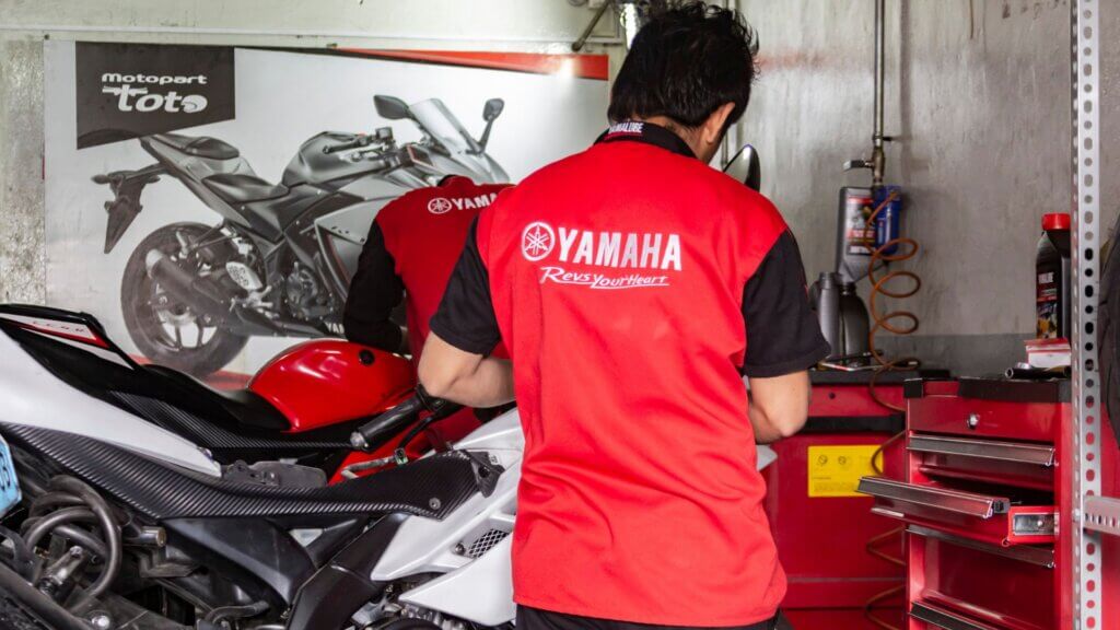 Yamaha technicians working on sport motorcycle inside company service workshop.