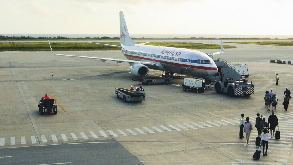 American Airlines plane at an airport gate as travelers walk across the tarmac.